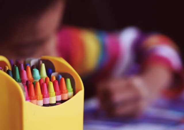 Crayons beside child colouring.