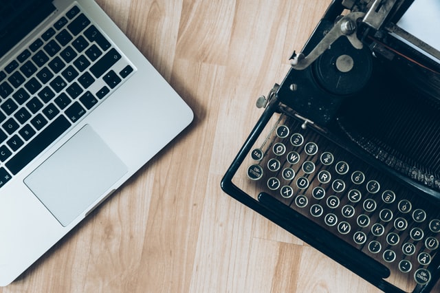 Partial view of laptop on left of desk and typewriter on right