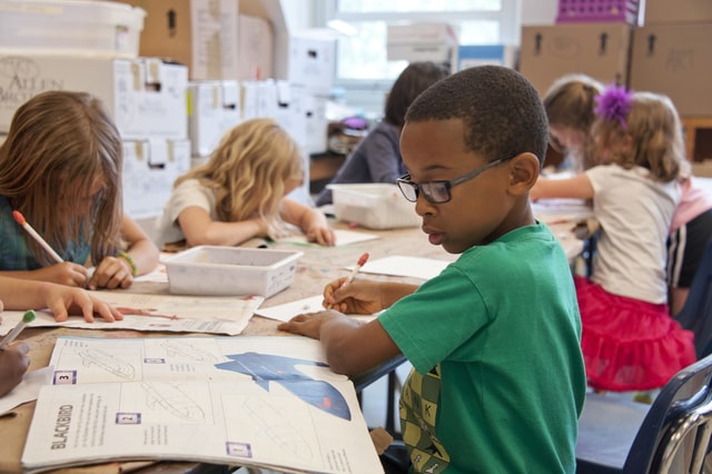 Boy reading and writing at school desk in classroom.