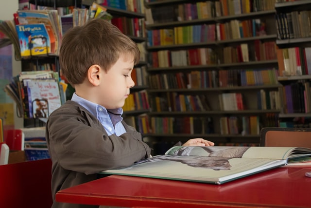 Young boy in school uniform sits at a desk in a library reading.
