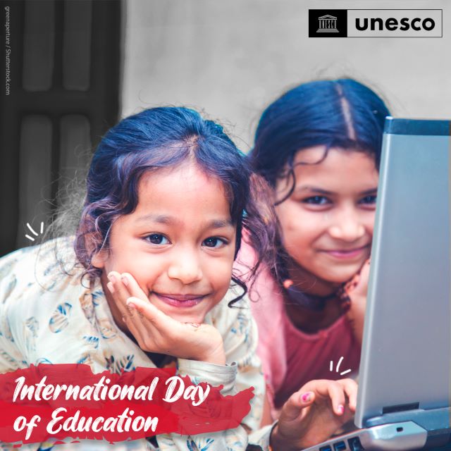 Two young girls smile at the camera from behind a computer screen. Banner text reads: International day of education