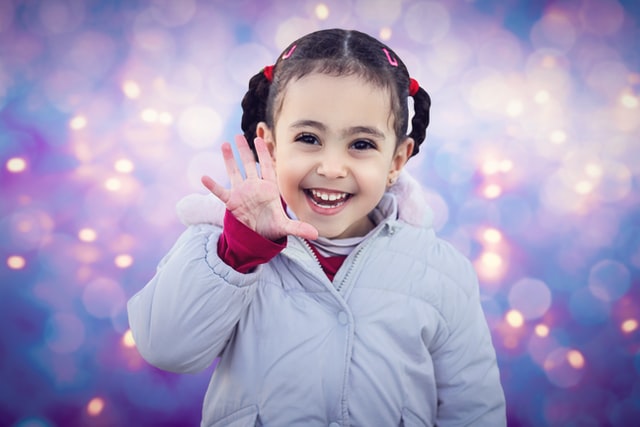 Young girl facing the camera and waving, against a glittery background