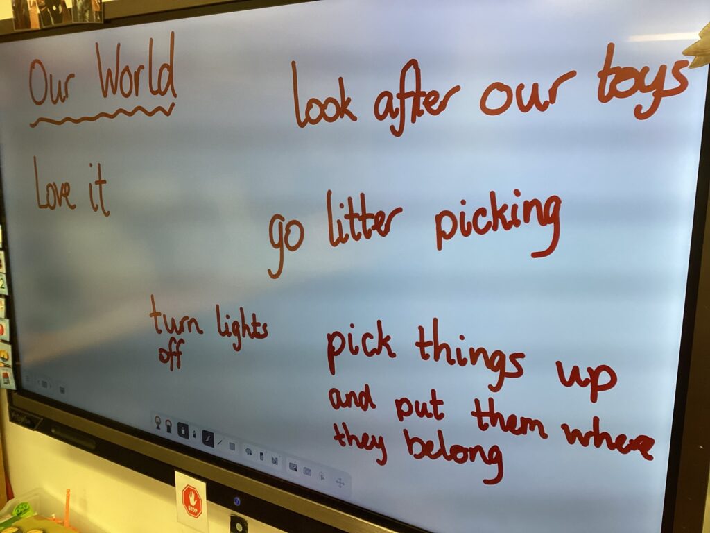 Classroom smartboard with heading Our World. Handwritten text dotted around the board as a brainstorm reads: Go litter picking. Turn lights off. Pick things up and put them where they belong. Look after our toys. 