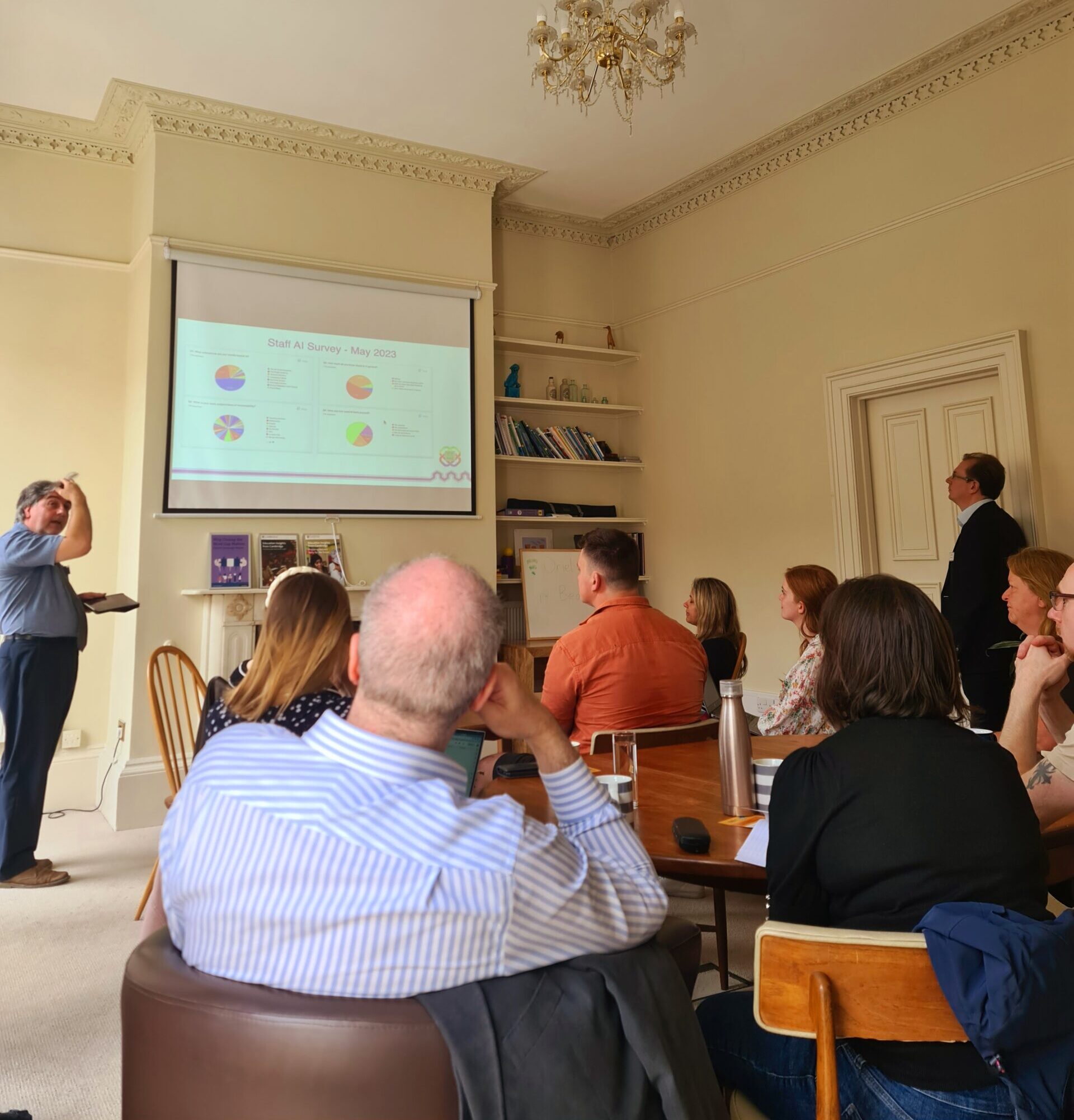 A group of adults sit facing a projector screen listening to a speaker.