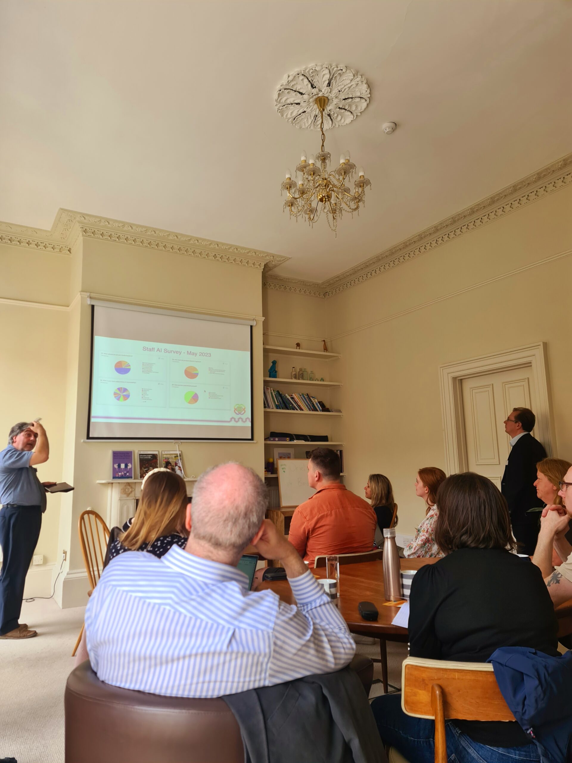 A group of training course delegates from the education industry  sit facing a projector screen listening to a speaker.