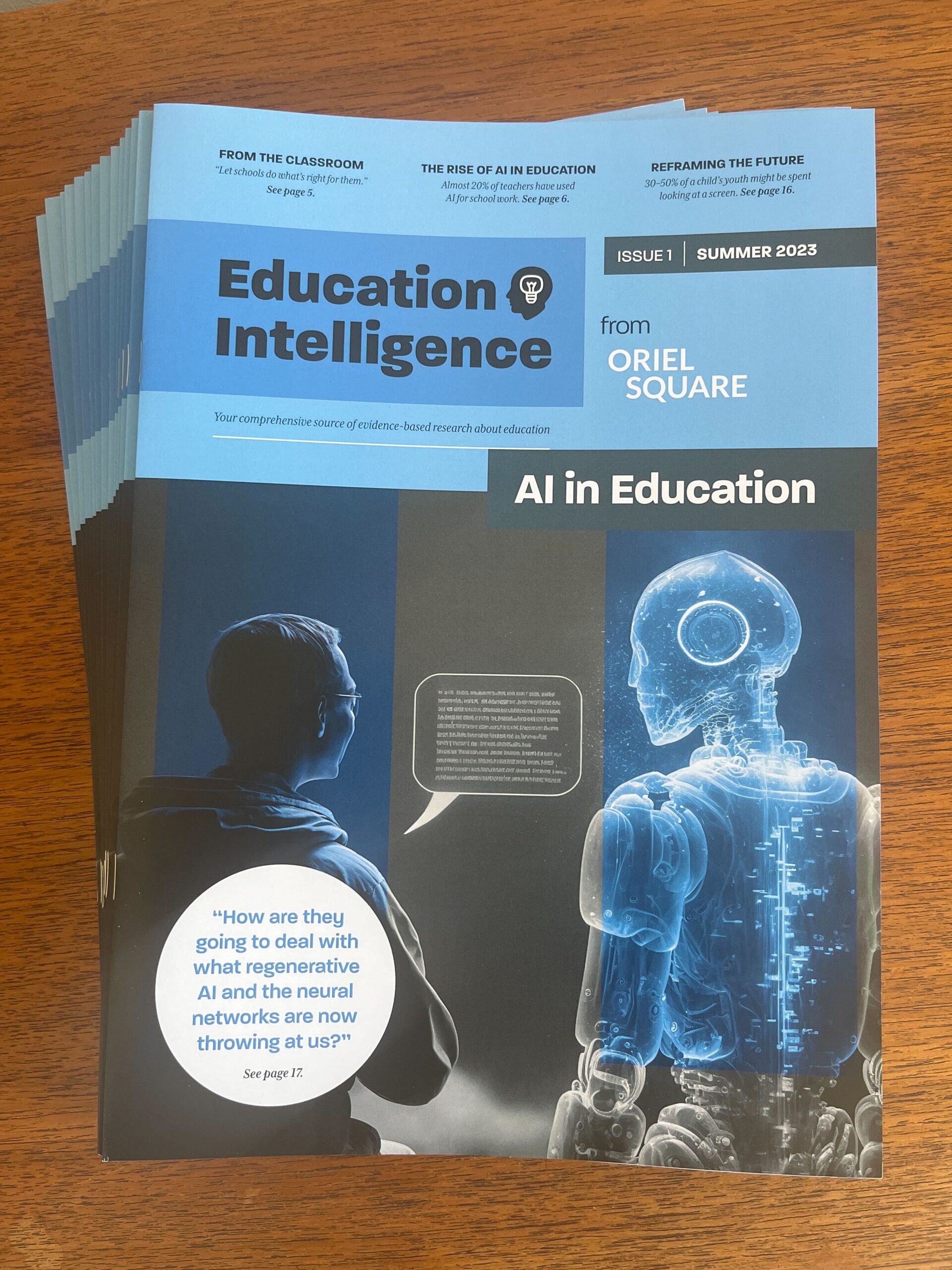 Printed reports stacked on a table. The report cover features an image of a student and a robot with the title Education Intelligence from Oriel Square: AI in education.