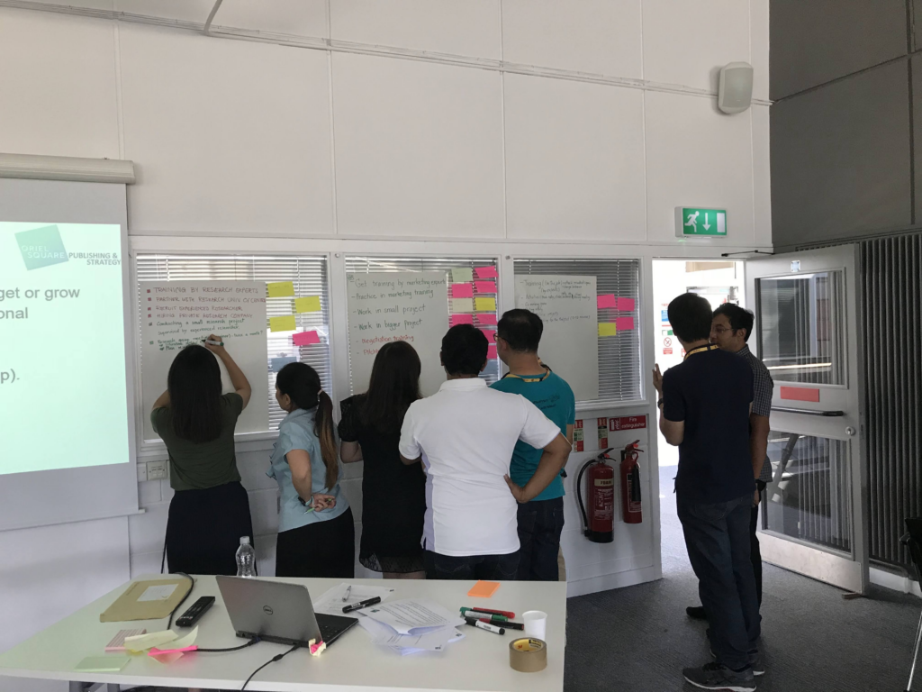 A group of training course delegates from the education industry looking at a board of post-it notes. 
